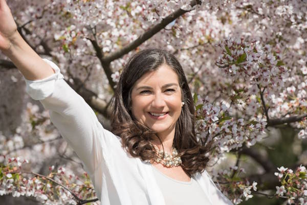 Susanne Schlenker von Schlenker Impulse steht vor einem Kirschbaum und winkt zur Begrüßung